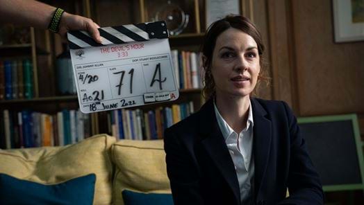 Jessica Raine on set of The Devil's Hour seated on a yellow sofa behind a clapper board