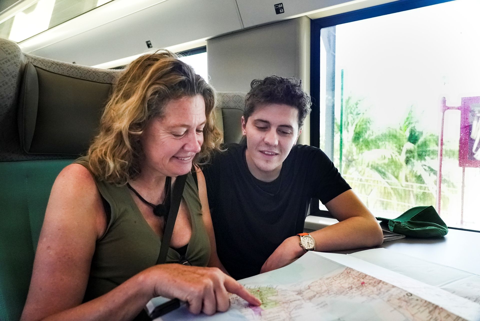 Two people sit at a table on a train looking at a map