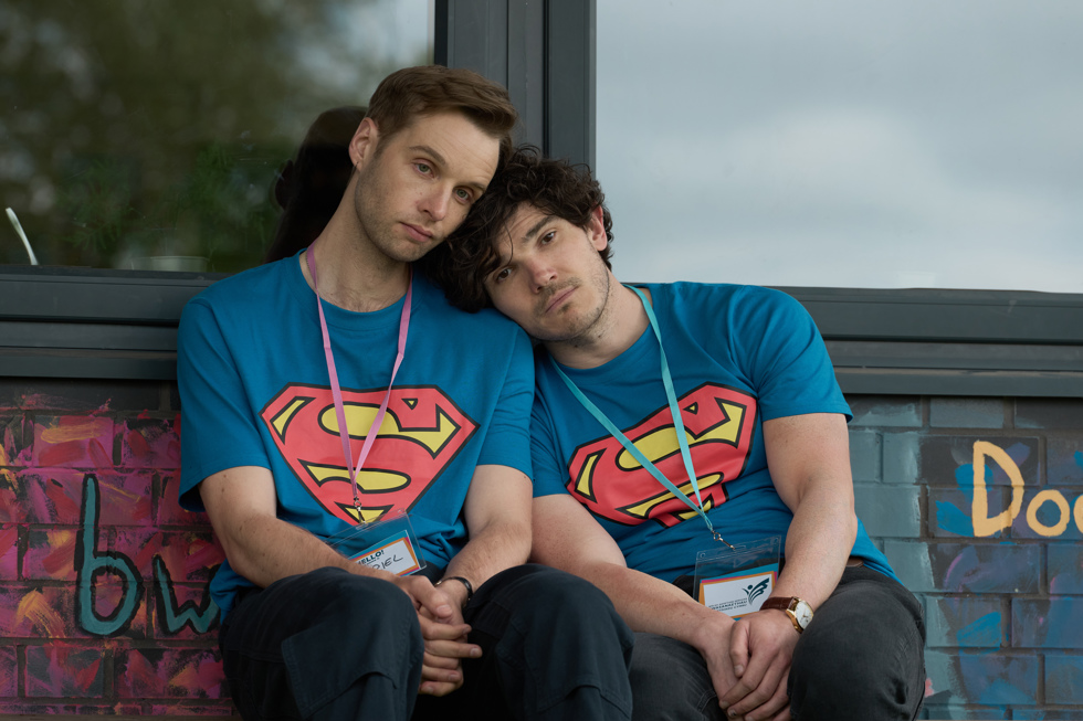 Production shot from Lost Boys and Fairies: two men in superman t-shirts lean on each other while sitting outside a building