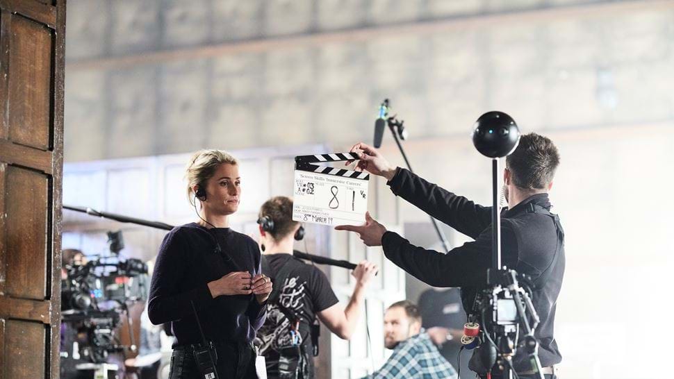 Man with clapper board stands in front of a woman wearing a headset with a 360 camera rig in the foreground