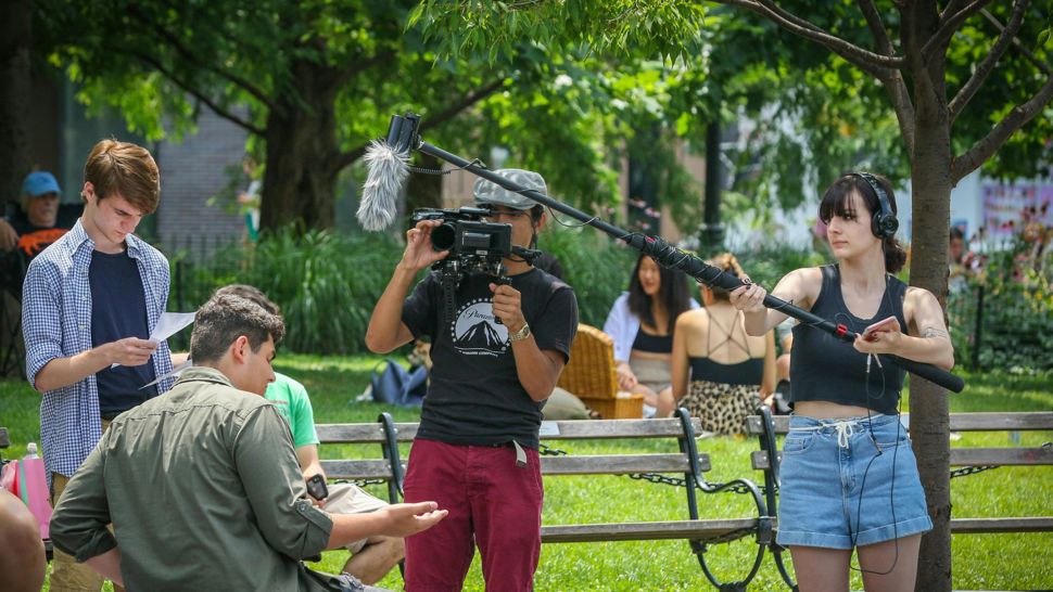Camera and sound crew filming a person sat on a park bench