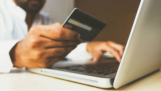 Close up of a person holding a credit card while typing on a laptop