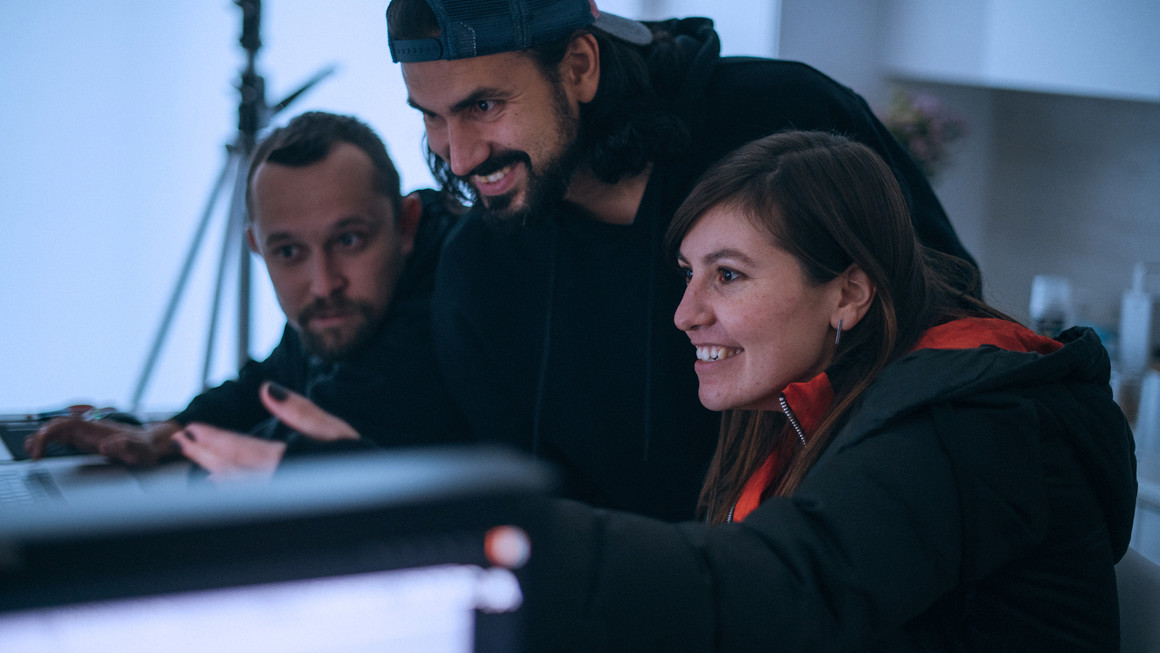 Two men and one woman smile as they watch a screen at a desk