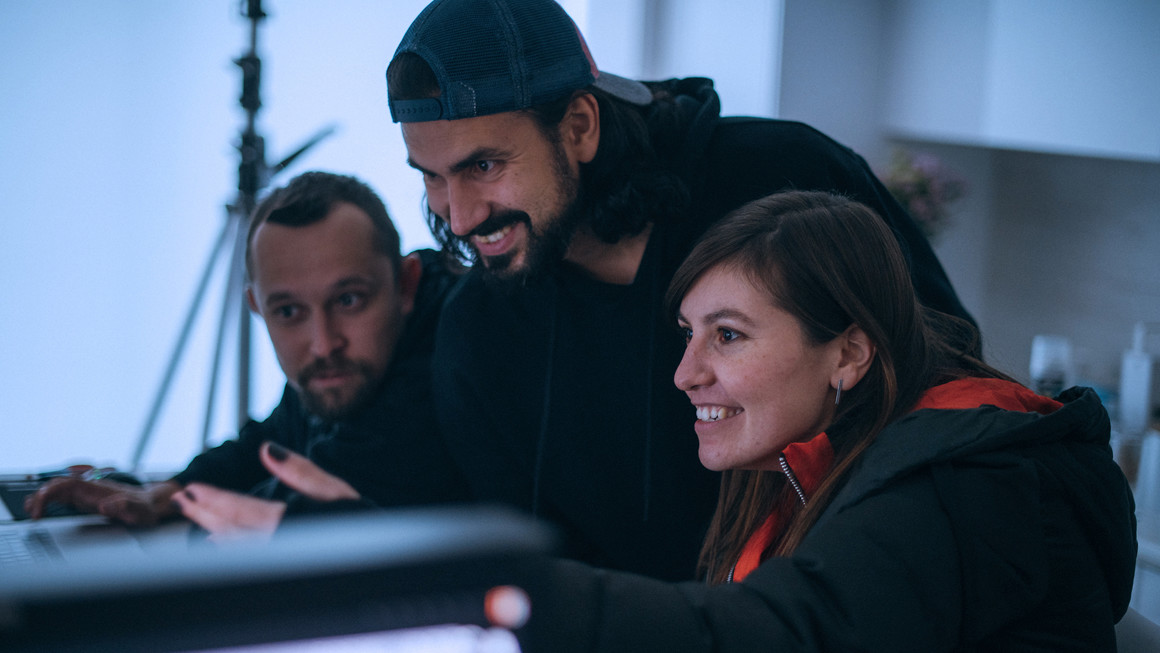 Two men and one woman smile as they watch a screen at a desk