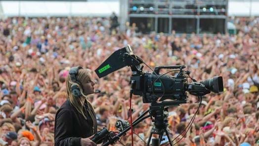 Female camera operator standing in front of a large outdoor crowd