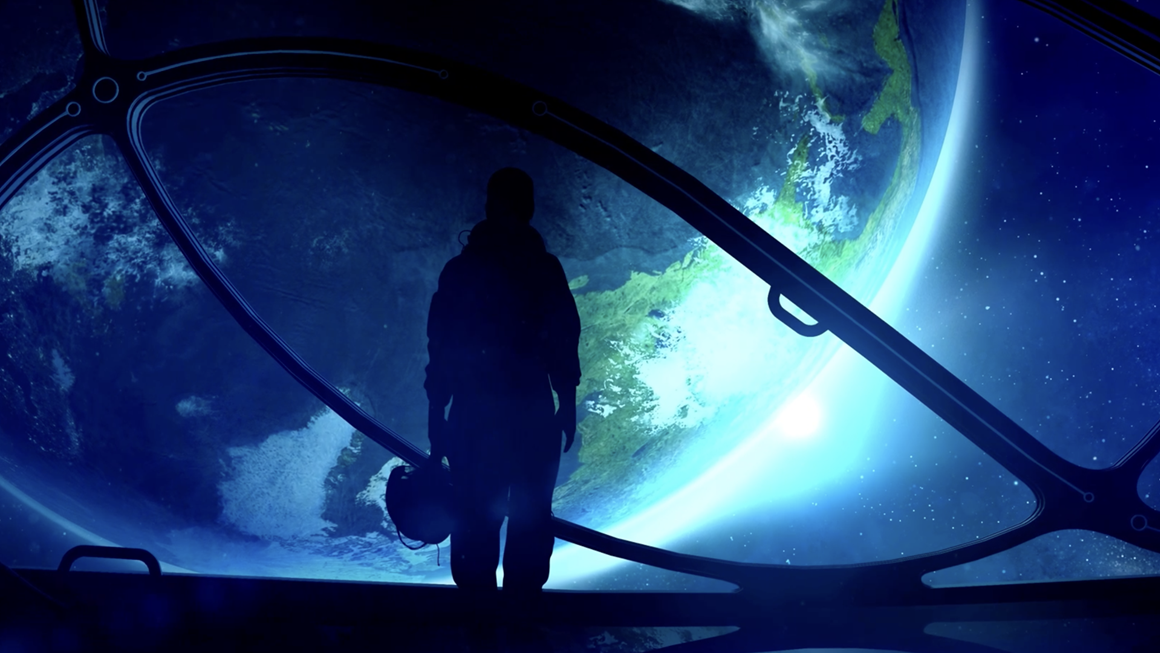 Dar image of a person holding a helmet in front of a large screen displaying an image of planet Earth from space