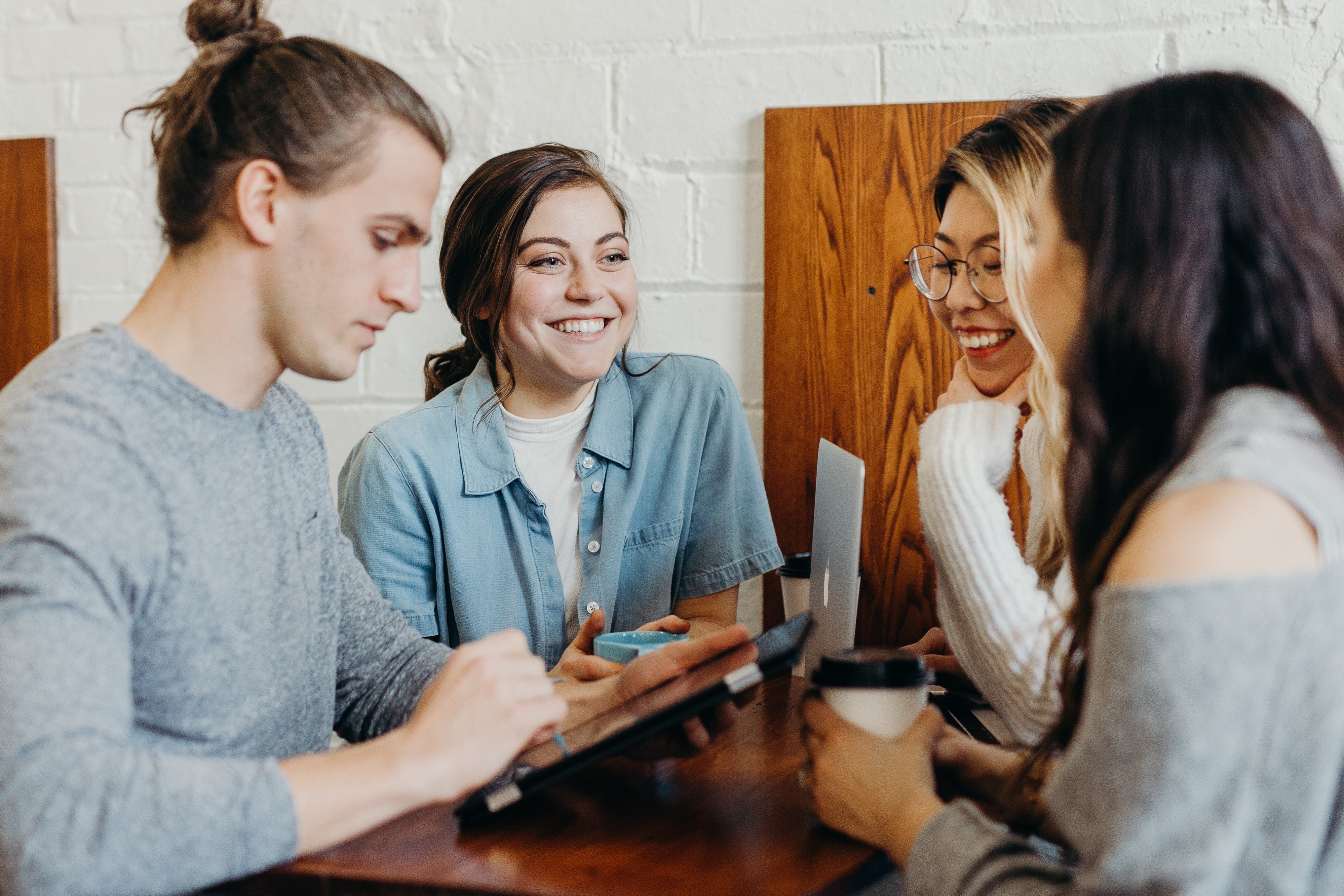 Group of young people standing with coffee around a laptop