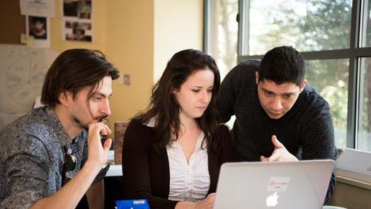 Three young people gathered around a laptop on a desk
