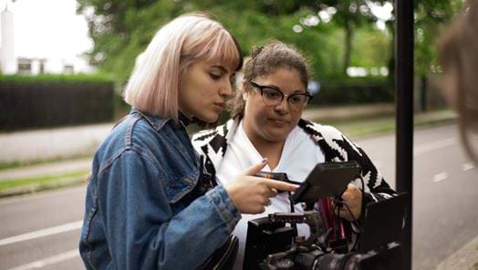 Two young women look at view finder on a television camera on location on a street