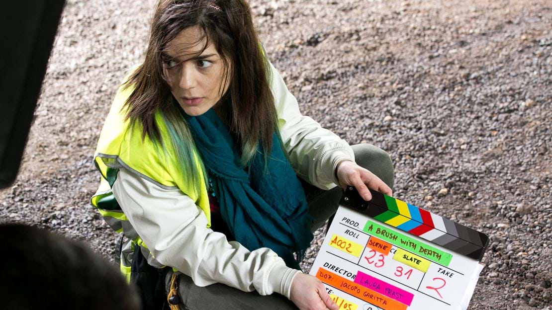 Woman crouching on the ground with a clapper board