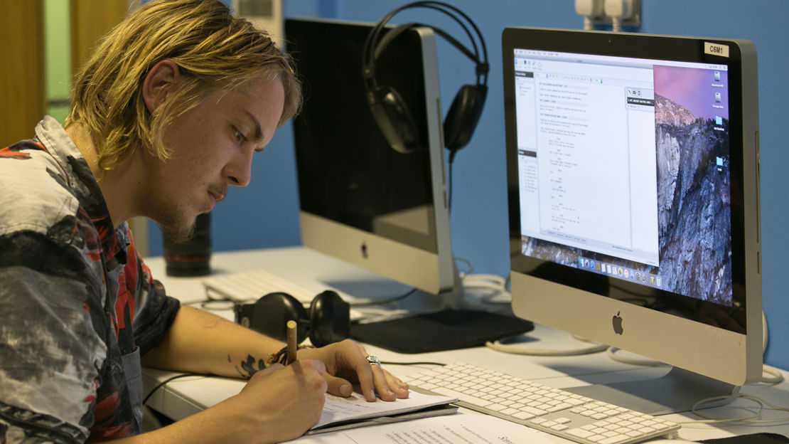 Man writing on a document in front of a computer screen