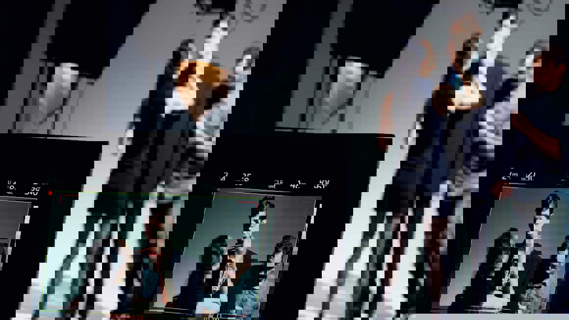 Camera viewer in the foreground showing a person applying make up to an actor and a man adjusting his costume, with the three people visible in the background