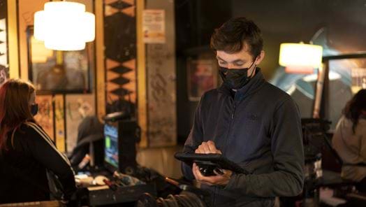A crew member is standing up holding a tablet while wearing a face mask