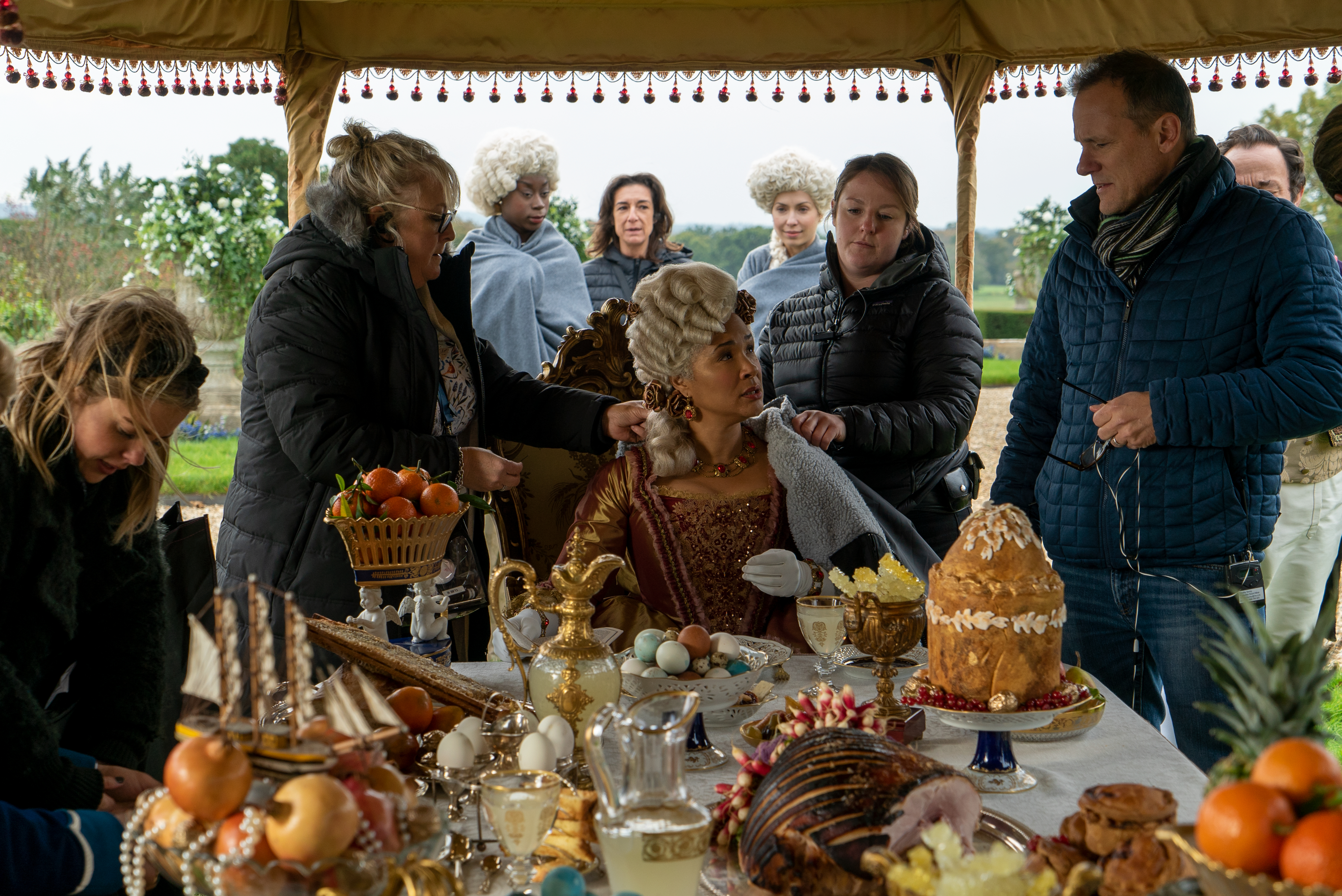 Behind-the-scenes image on the set of Bridgerton filming an outdoor feast in full costume