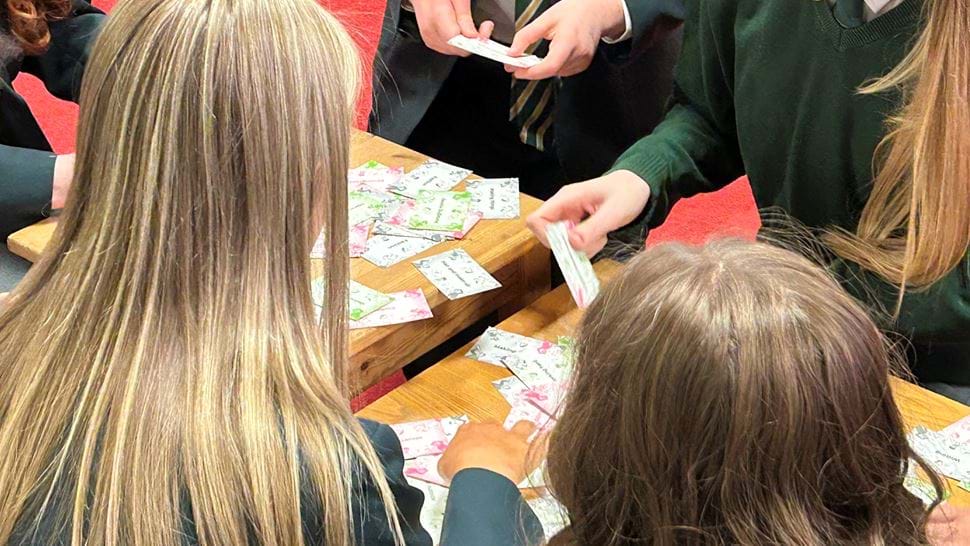 School children in uniform work around a table with note cards