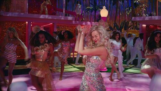 Margot Robbie (as Barbie) dancing at a party with fellow Barbies in the background