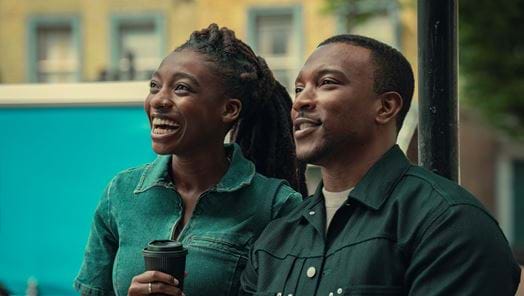 Simbi Ajikawo aka Little Simz (as Shelley) & Ashley Walters (as Dushane) stand next to each other smiling in production shot from Top Boy Season 3