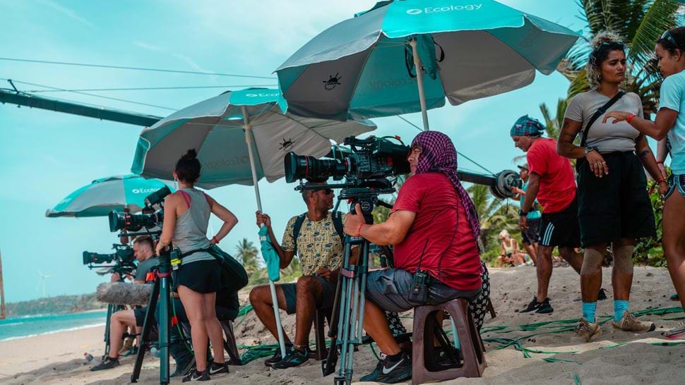 Crew filming under umbrellas on a beach on the set of Survivor
