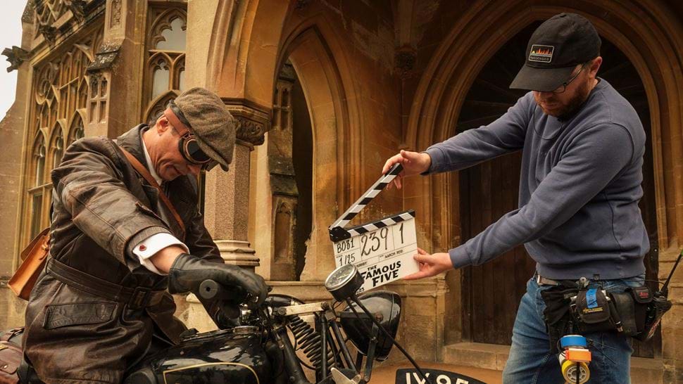 Behind-the-scenes production still of actor on a motorbike in front of a clapper board
