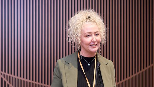 Hair and make-up artist Melanie Doyle stands at a podium giving a presentation