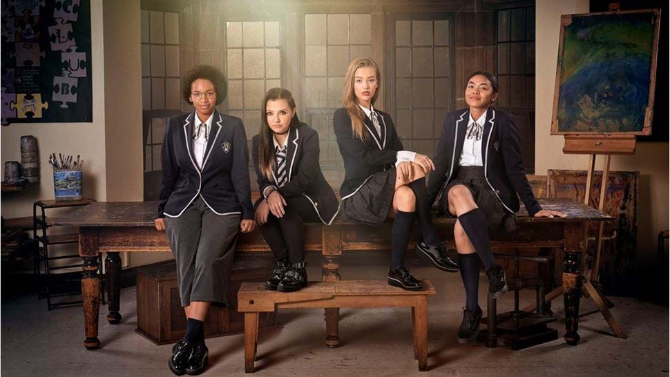 Get Even production shot of four young women in school uniform sitting on a desk in an old fashioned classroom