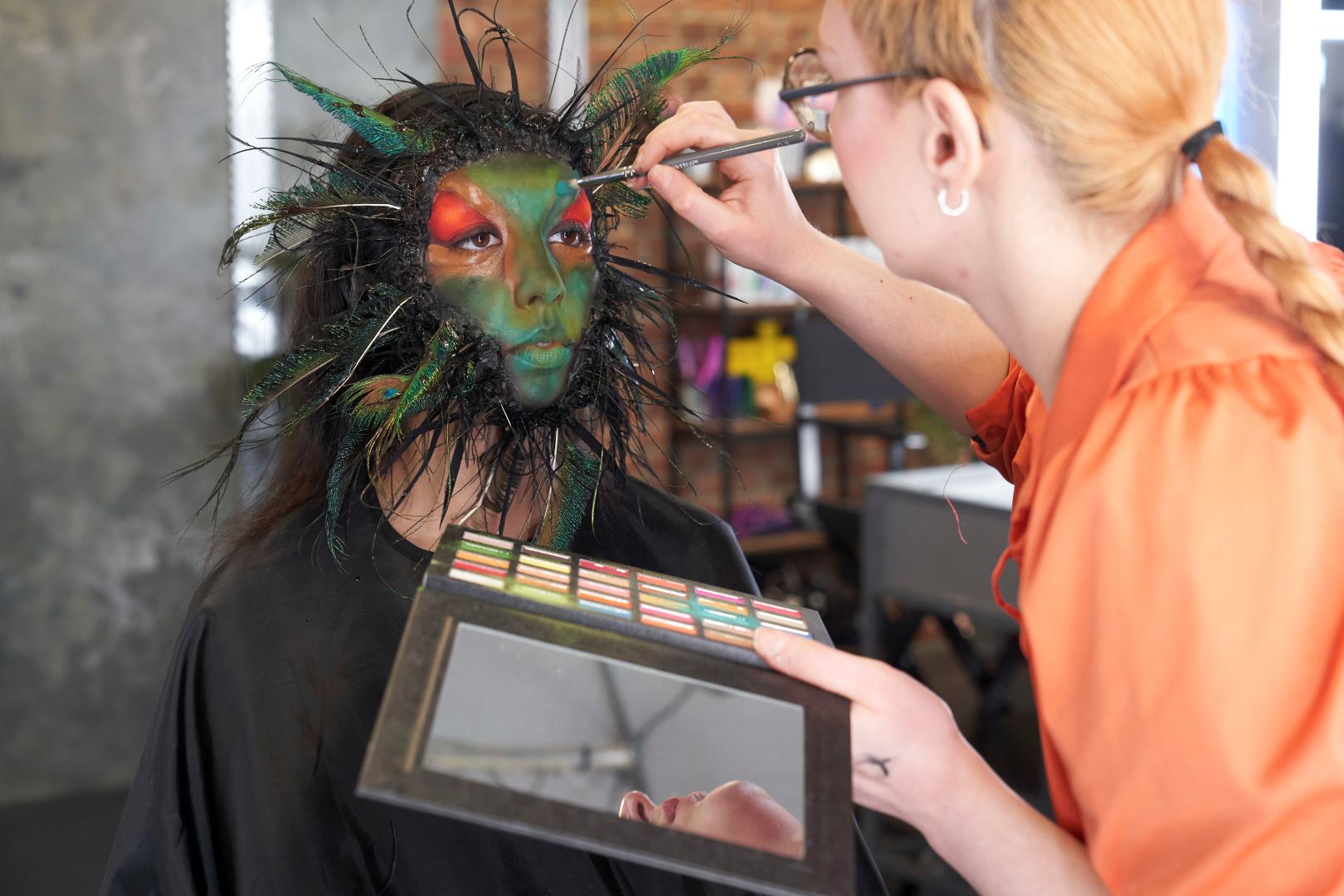 Behind-the-scenes of a make-up artist applying colourful make-up and feathering around the face