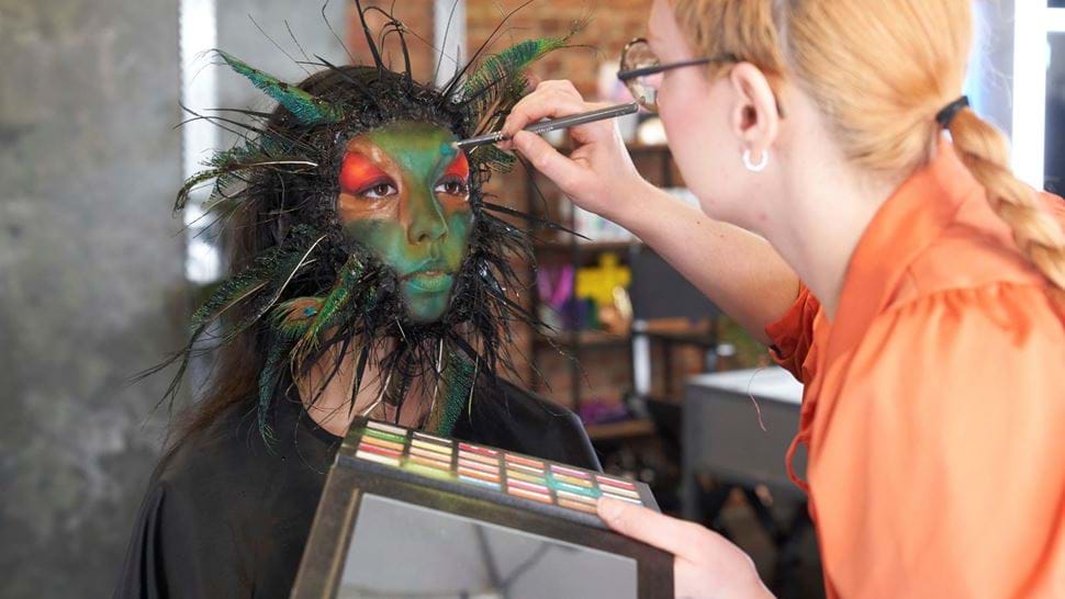 Behind-the-scenes of a make-up artist applying colourful make-up and feathering around the face