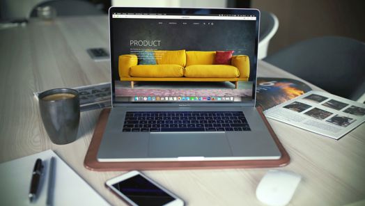 A laptop on a work desk displaying a web page with a bright yellow sofa indicating online shopping