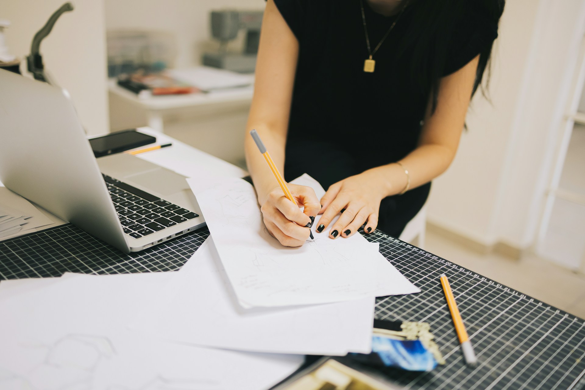 A closeup of a desk where someone is seen writing on sheets of paper next to an open laptop