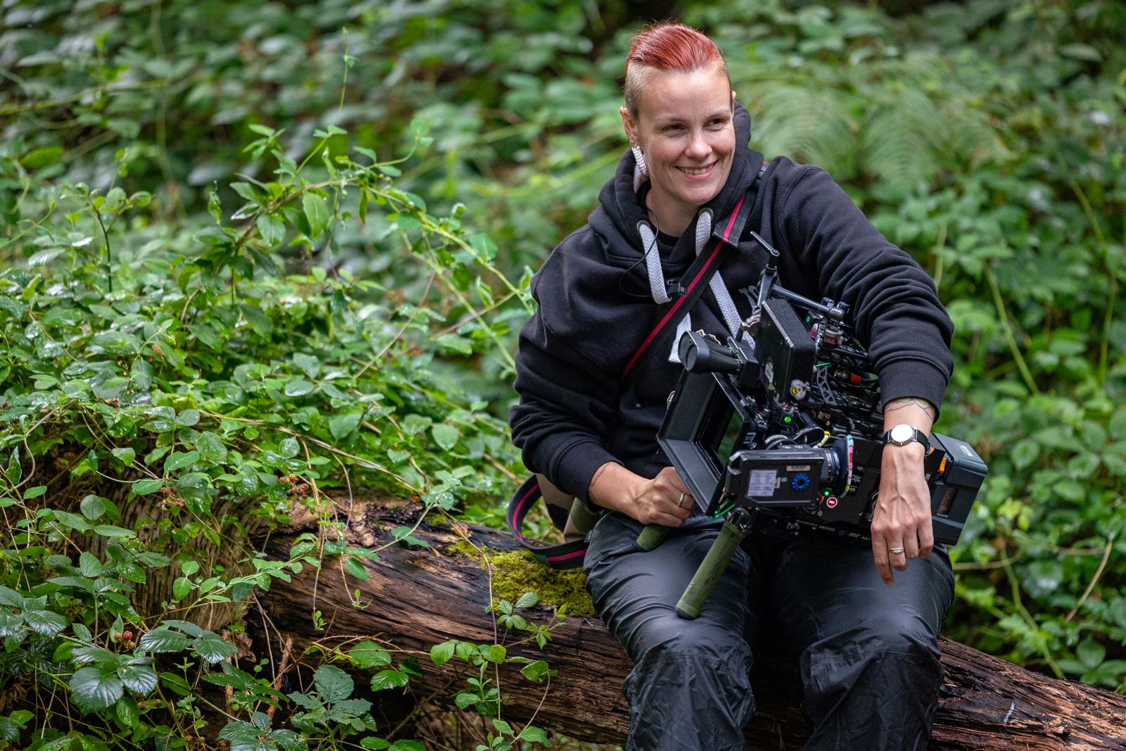 Maja Jensen smiles as she sits in a wooded area holding a large camera