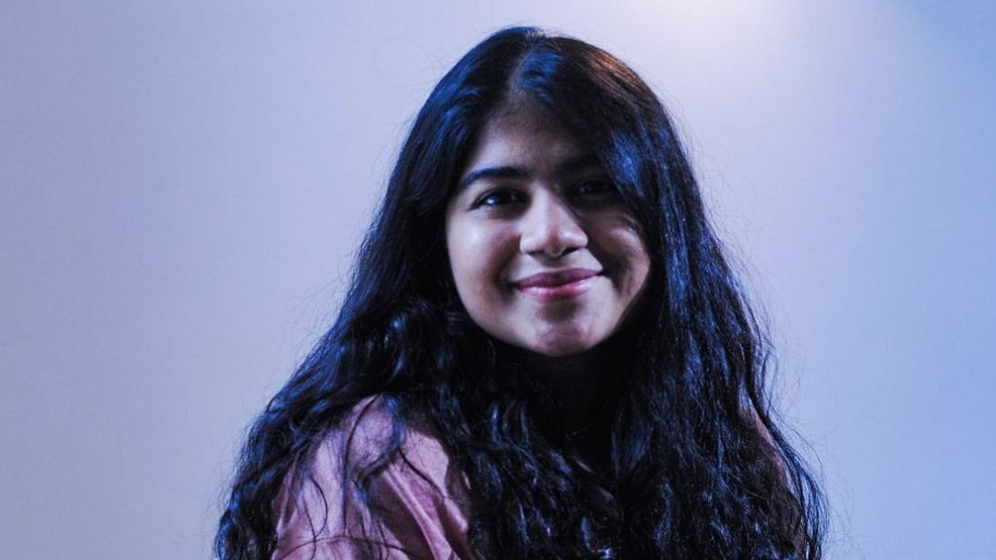 A headshot of Sanjoli Malani smiling towards the camera in front of a pale plain background