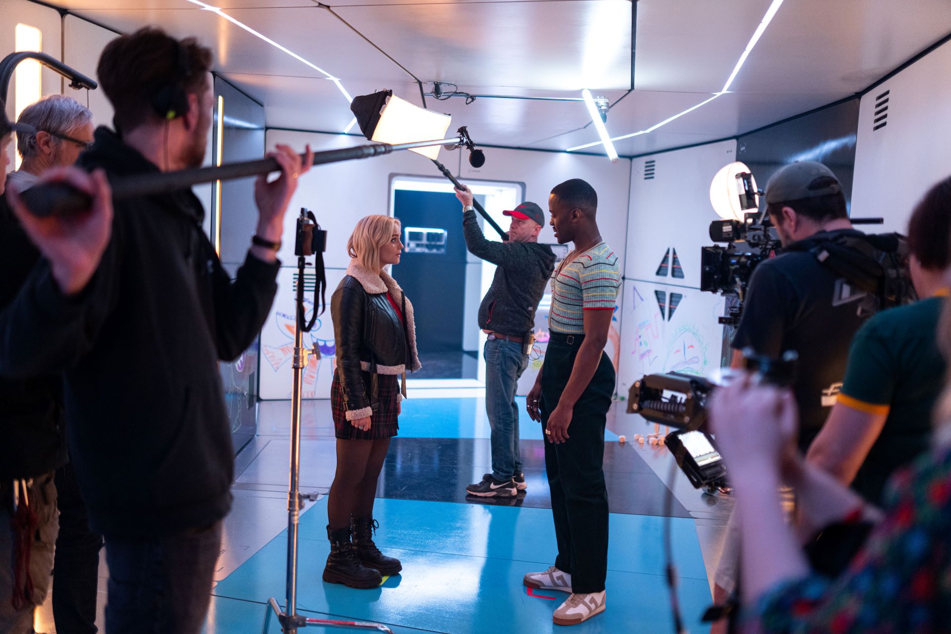 On the set of Doctor Who, Ncuti Gatwa as the 15th Doctor stands facing Millie Gibson as Ruby Sunday surrounded by production crew