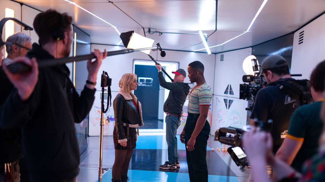 On the set of Doctor Who, Ncuti Gatwa as the 15th Doctor stands facing Millie Gibson as Ruby Sunday surrounded by production crew