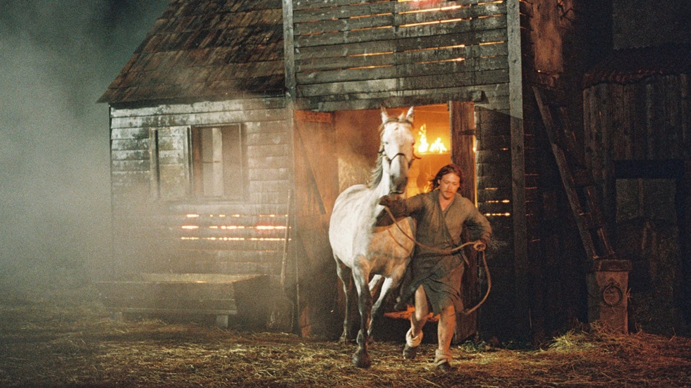 A running man leads a horse from a burning barn