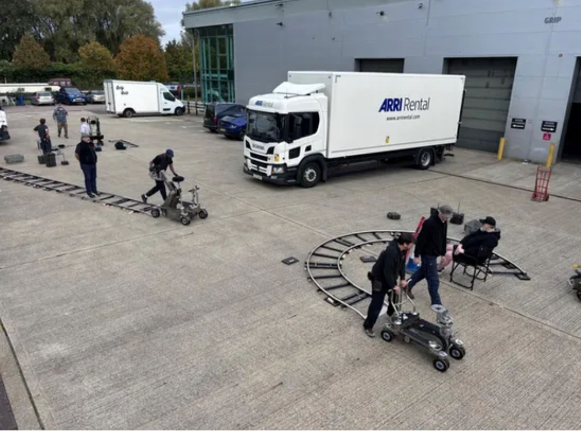 A warehouse car park with several cars and vans parked and a team operating two dollies