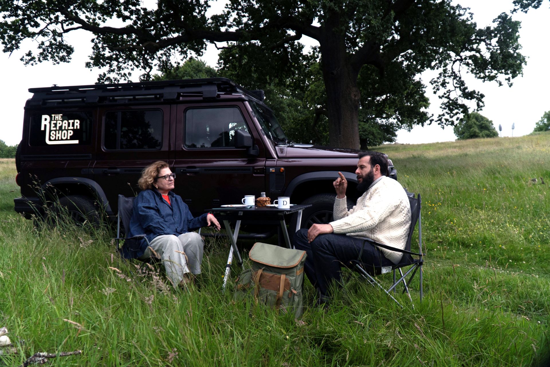 Hosts of The Repair Shop on the Road, Lucia and Dom, sit in a field by a vehicle