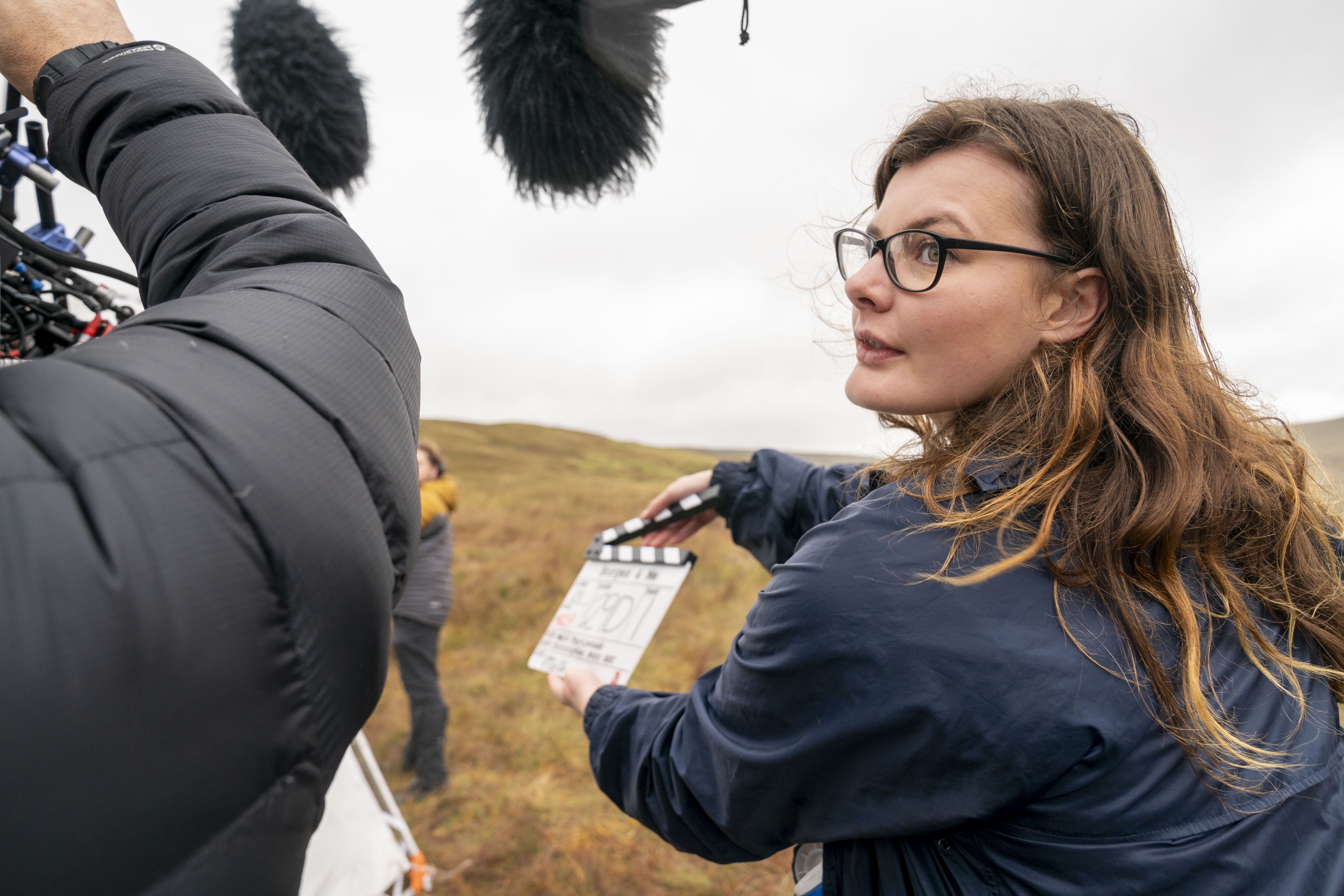 A person holds a clapperboard while another person operates an overhead microphone
