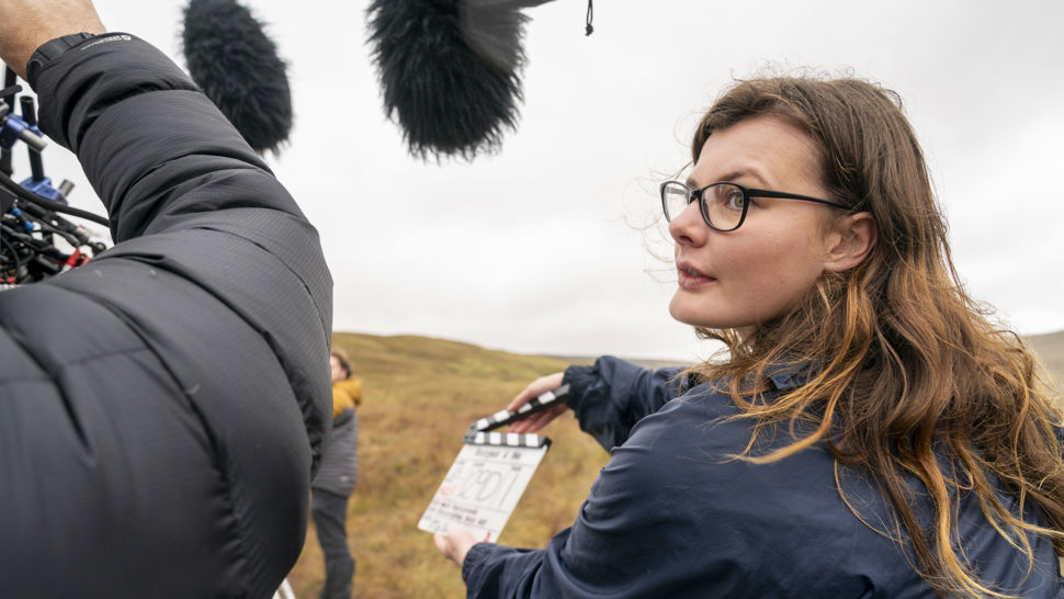 A person holds a clapperboard while another person operates an overhead microphone