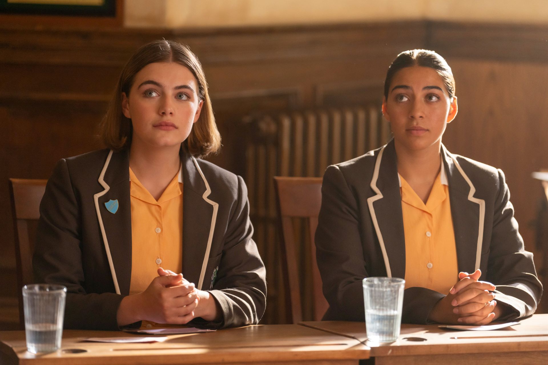 Two girls in school uniform sit side by side at a table