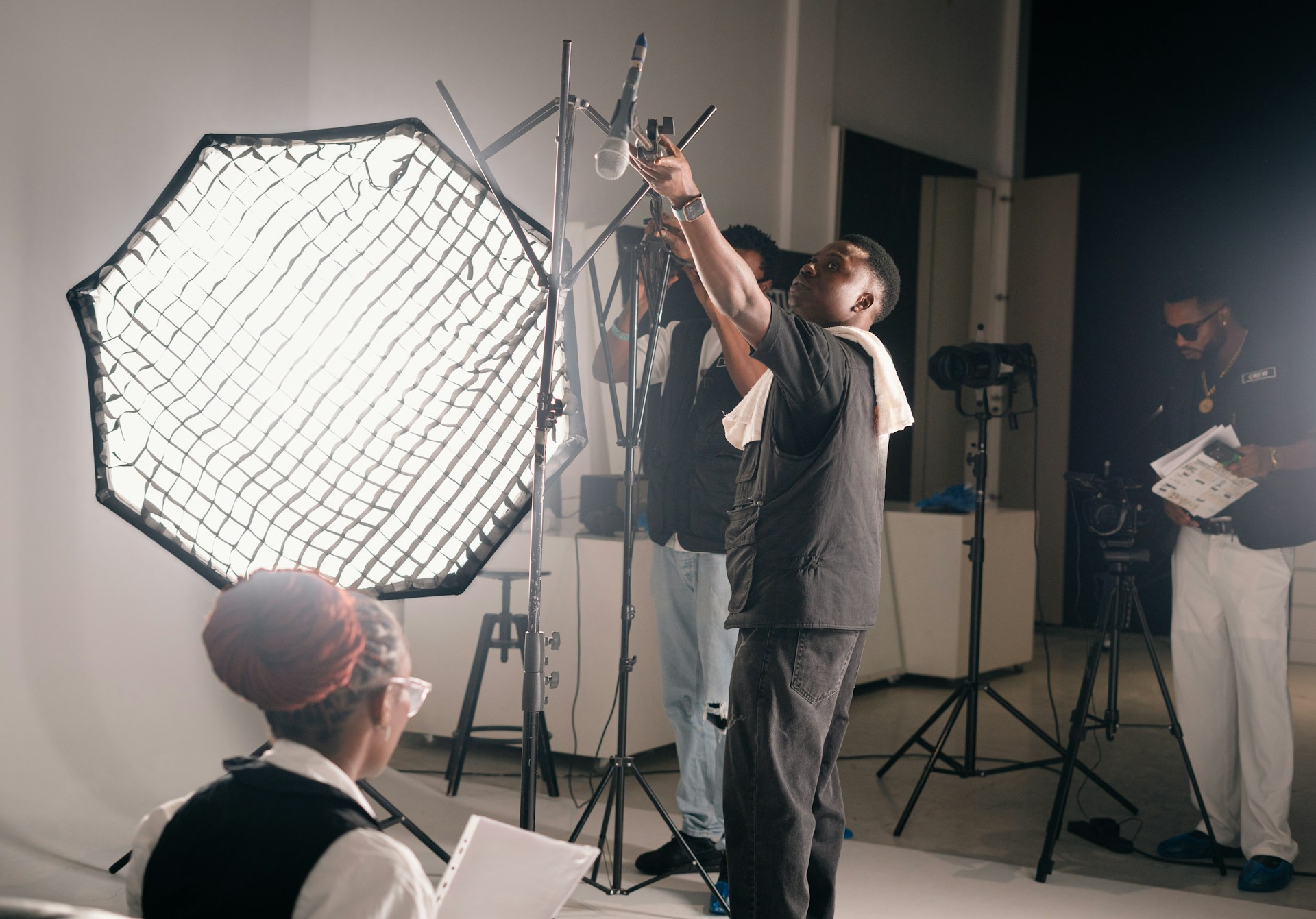 A man stands adjusting a microphone stand on set