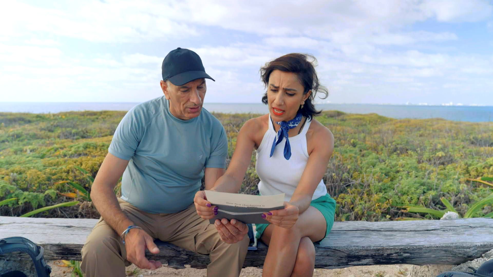 Two people sit on a bench looking at a letter
