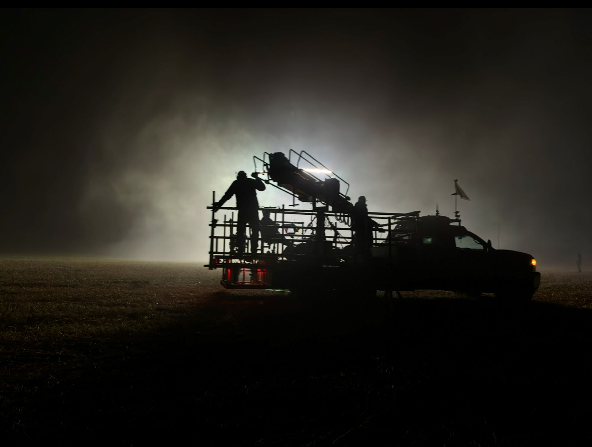 A crew operates a crane grip on the back of a truck during a night-time scene
