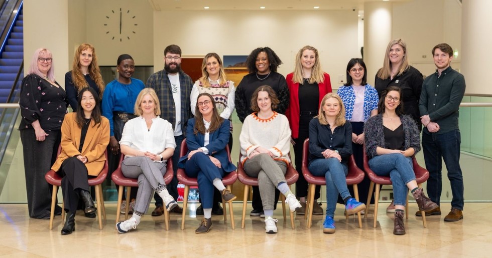 16 candidates pose for a group photo. Ten members stand behind six seated members as they smile at the camera