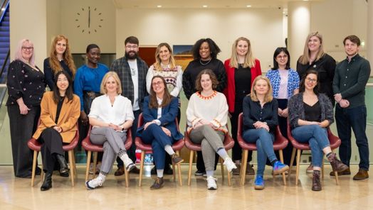 16 candidates pose for a group photo. Ten members stand behind six seated members as they smile at the camera